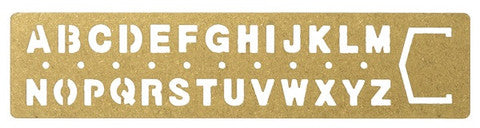 brass alphabet ruler with letters A to Z on a beige background.