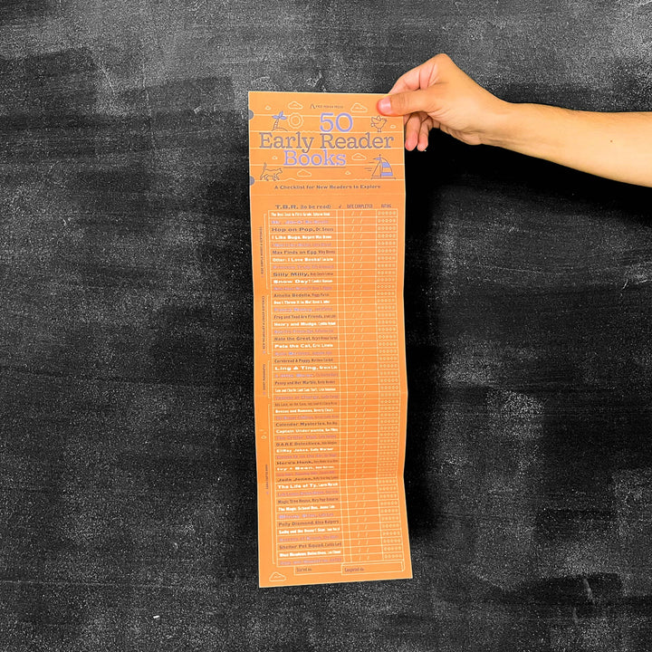 Hand holding a list of 50 Early Reader Books against a dark textured background