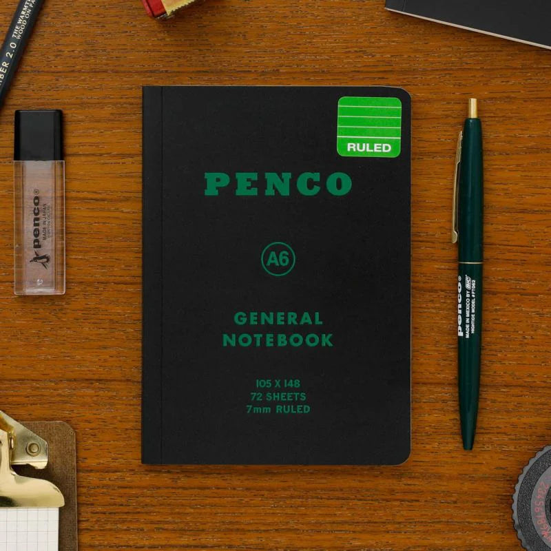 Penco notebook on a wooden surface with a pen and other stationery items.
