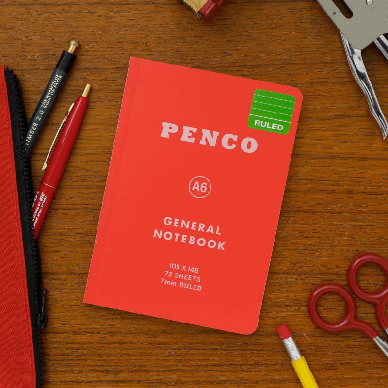 Red Penco notebook on a wooden surface with stationery items.