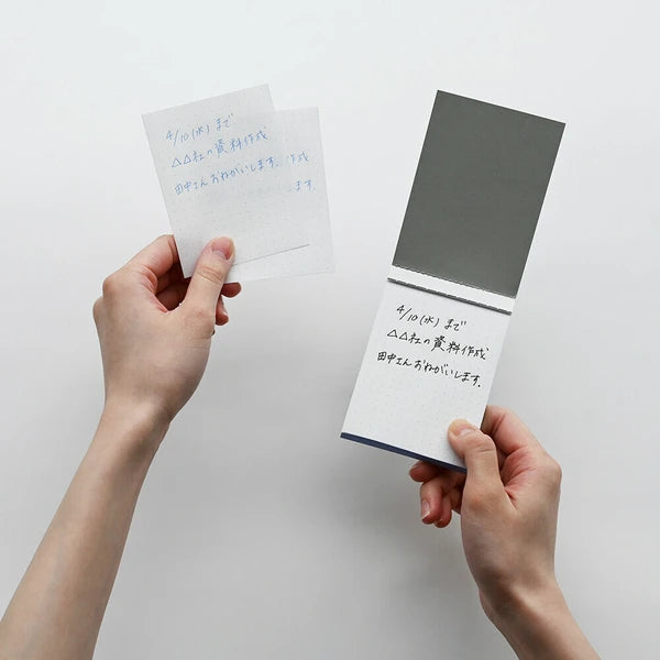 Two hands holding small notebooks with handwritten text on a white background