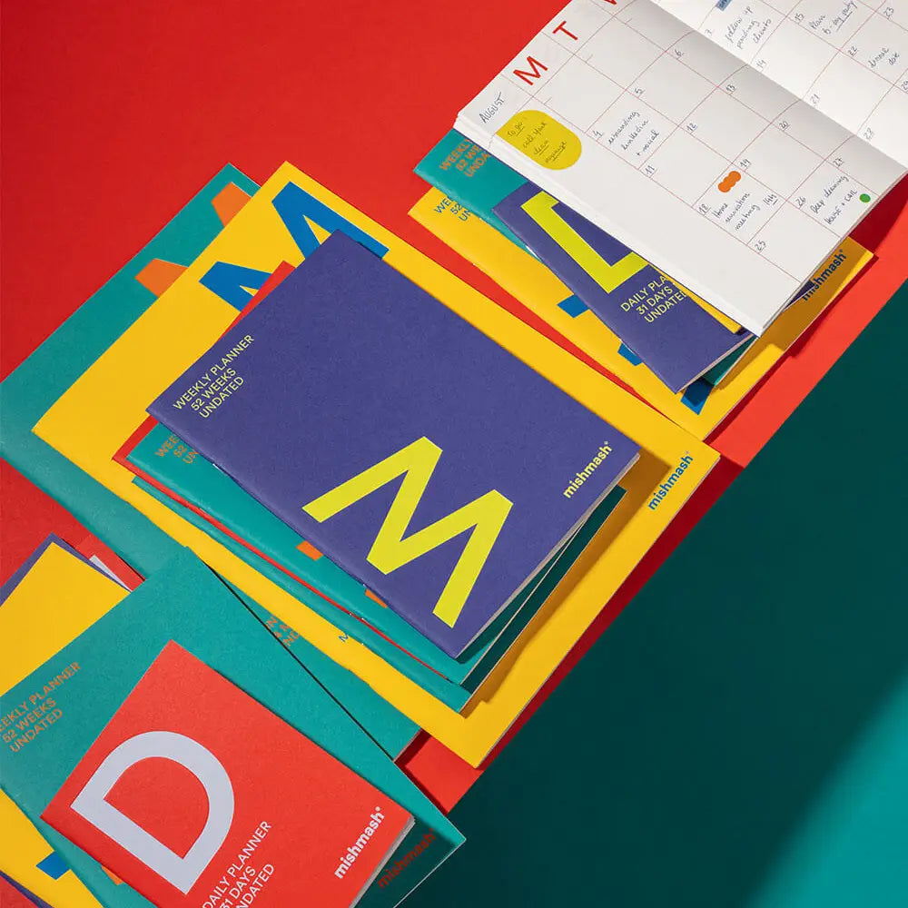 Colorful planner books with 'M' branding on a red and blue gradient background