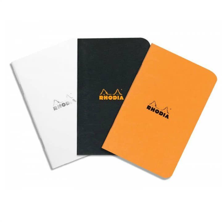 Three Rhodia notebooks in white, black, and orange on a white background