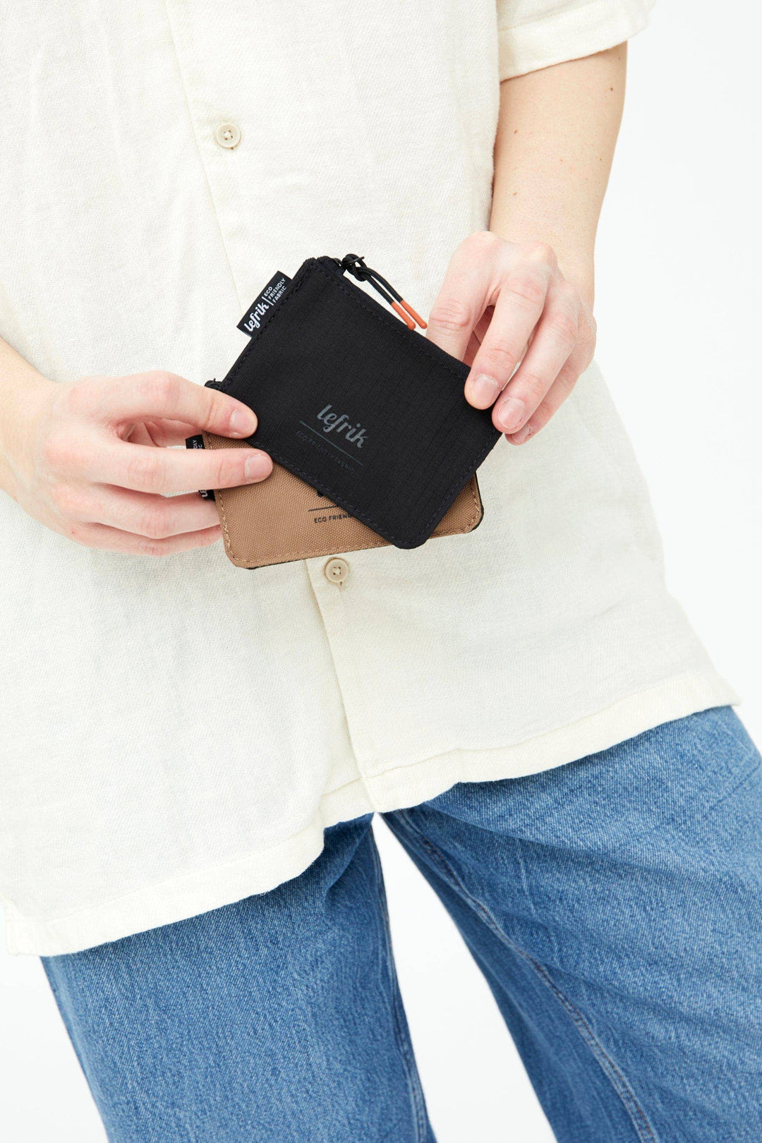 Person holding a black zippered pouch with 'Lefrik' branding, wearing a white shirt and blue jeans.