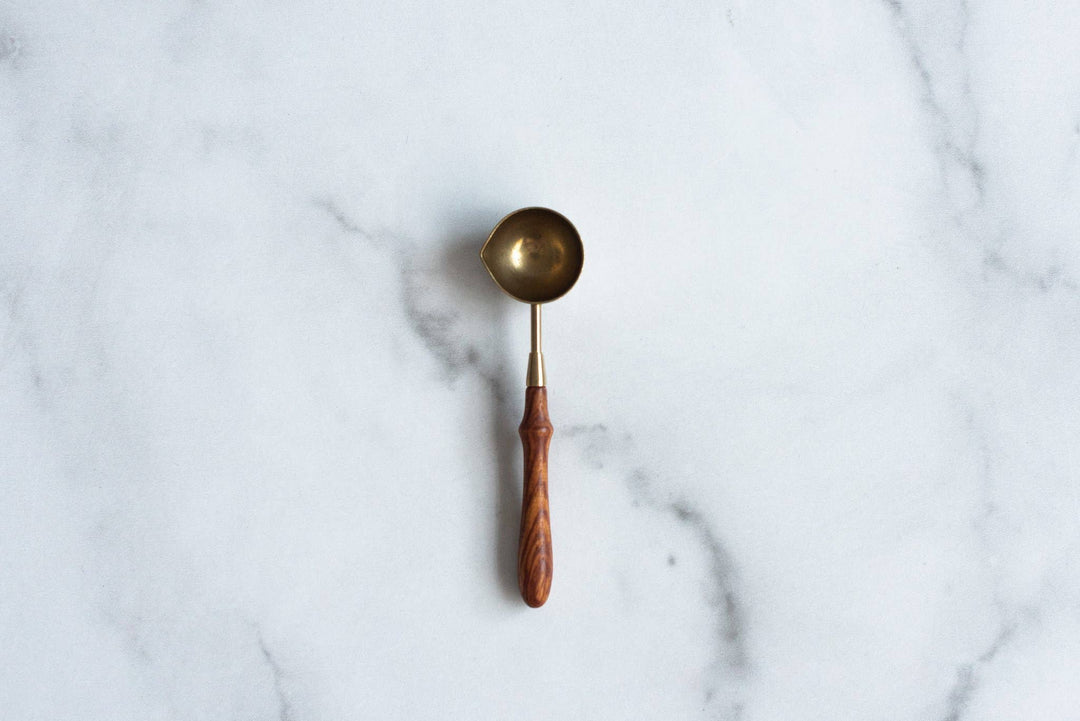 Brass wax melting spoon with wooden handle on a marble surface