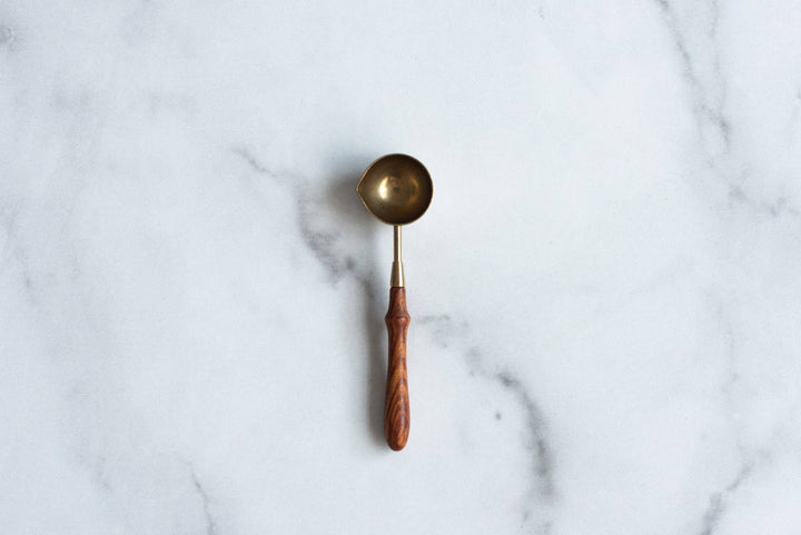 Brass wax melting spoon with wooden handle on a marble surface