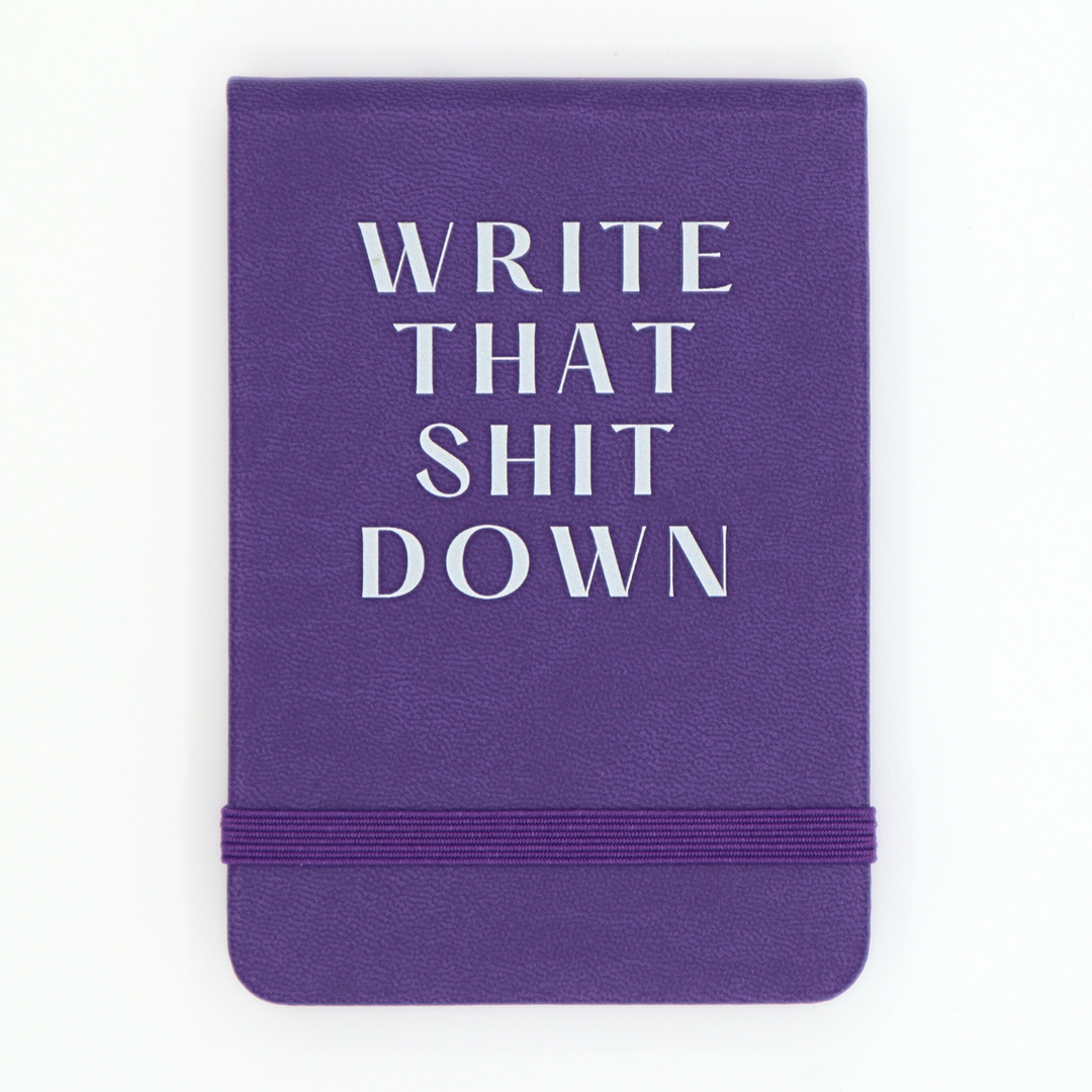 Purple notebook with white text 'WRITE THAT SHIT DOWN' on a white background