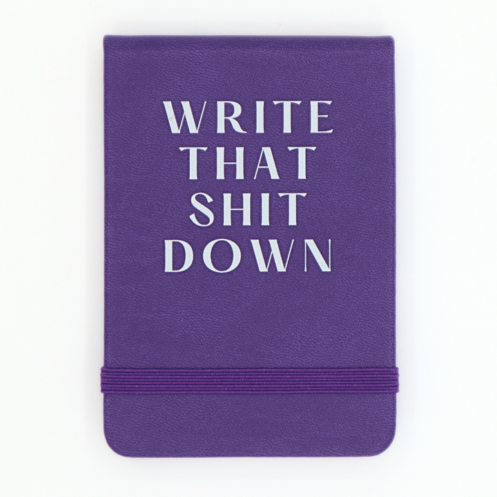 Purple notebook with white text 'WRITE THAT SHIT DOWN' on a white background