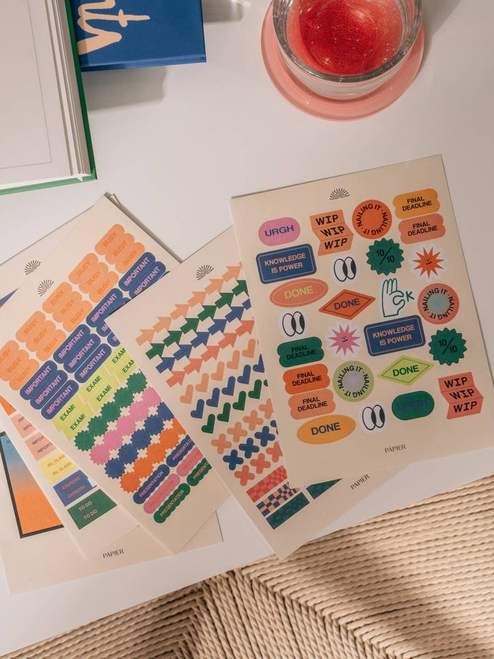 Two sheets of colorful stickers on a textured surface with a candle in the background.