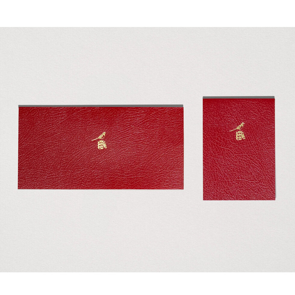 Two red leather-bound books with gold embossed designs on a white background.