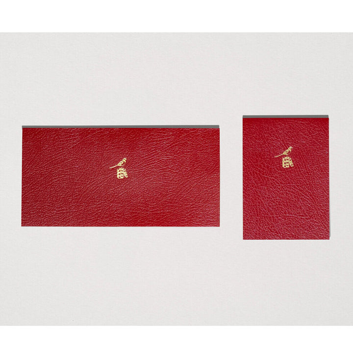 Two red leather-bound books with gold embossed designs on a white background.
