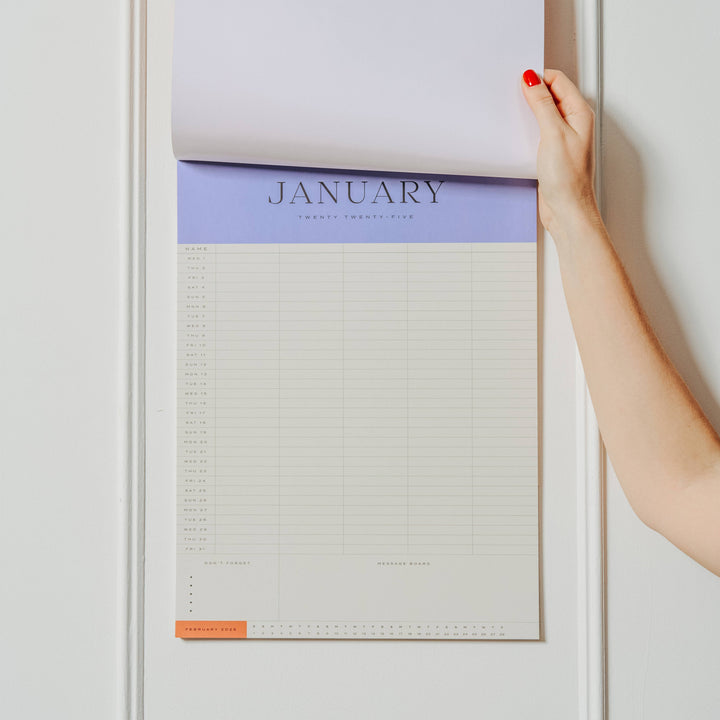 Calendar with January on a white wall, held by a hand.