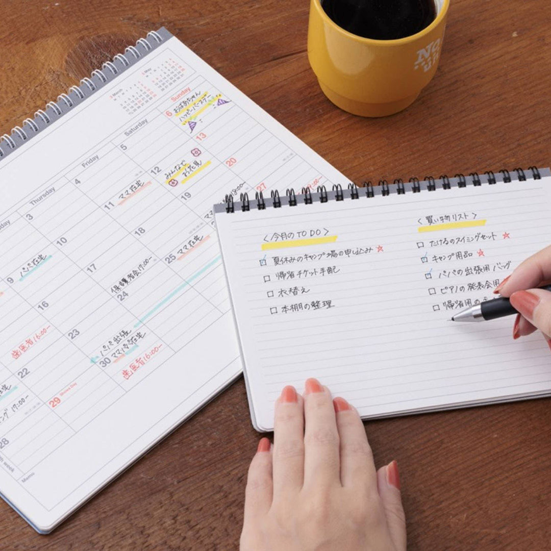 Person using a planner with a yellow mug on a wooden table