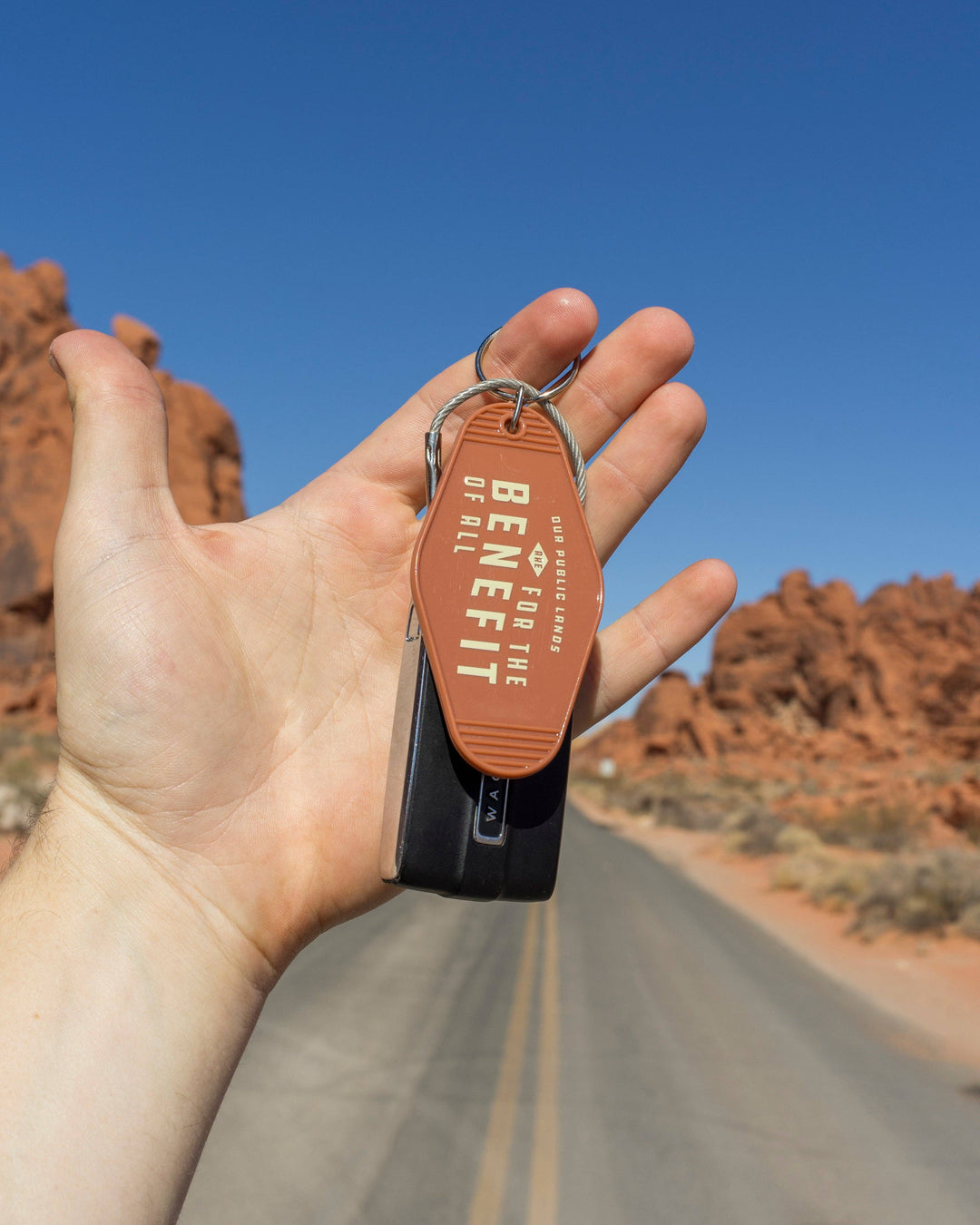 Hand holding a keychain with 'Benefit' branding against a desert landscape.
