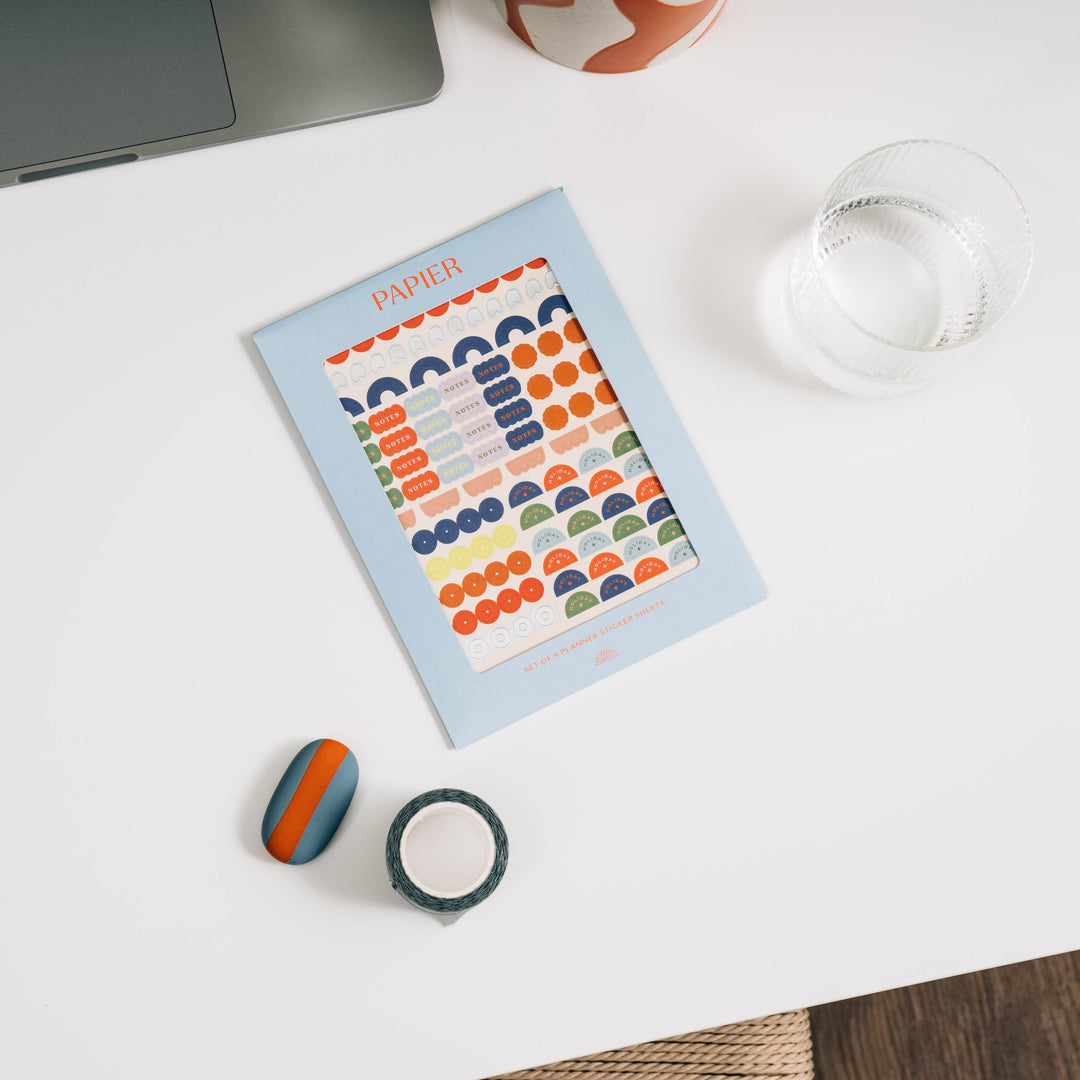 Colorful sticker sheets and stationery items including a notebook, tape, and rubber on a white surface.