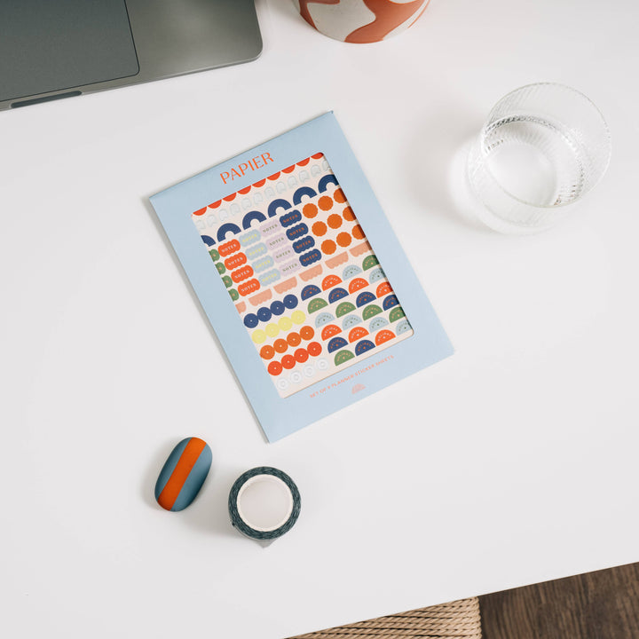 Colorful sticker sheets and stationery items including a notebook, tape, and rubber on a white surface.