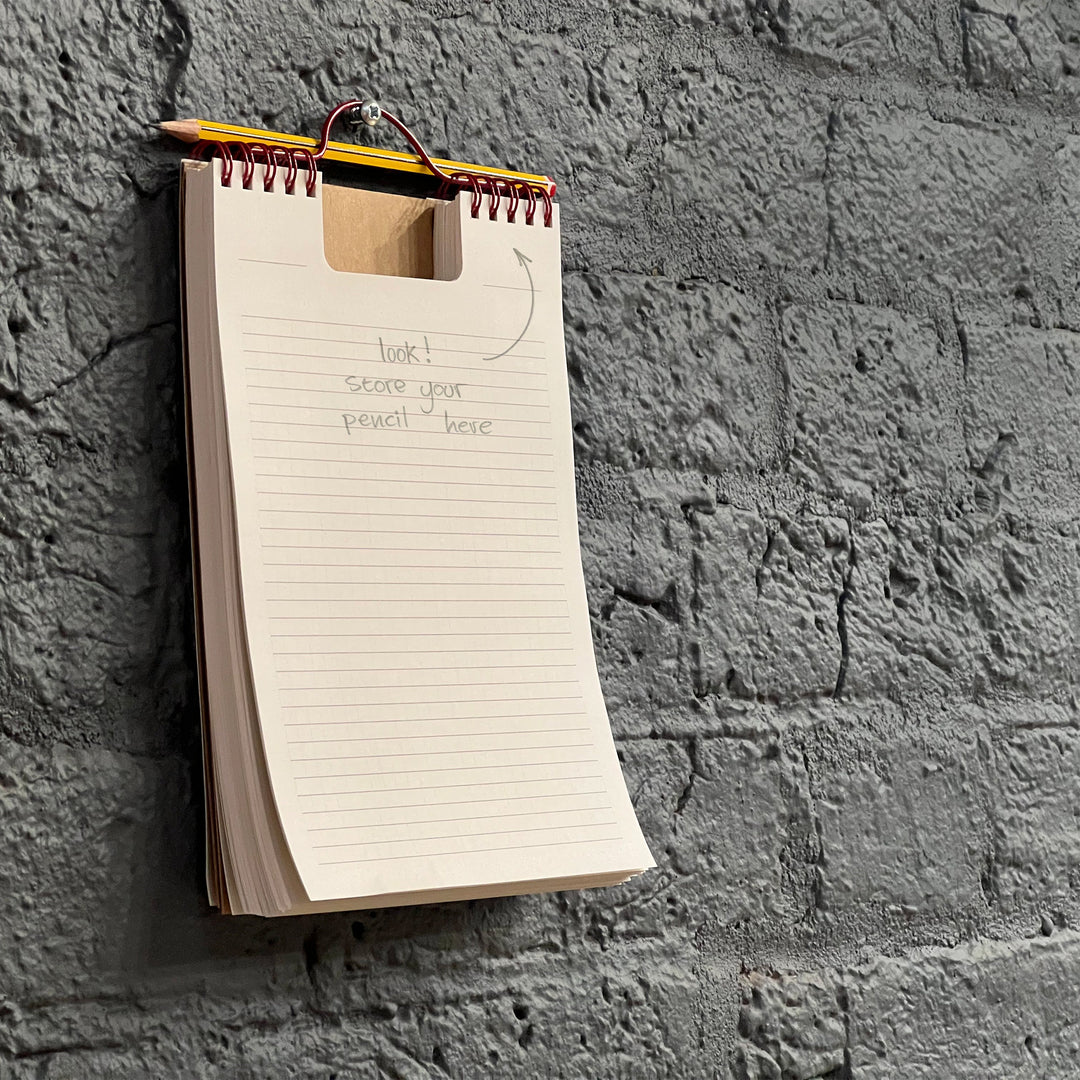 Notebook with wooden cover and pencil attached to a textured gray wall