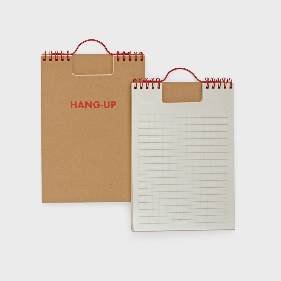 Two spiral-bound notebooks, one brown with 'HANG-UP' text and one white with lined pages, on a light gray background.