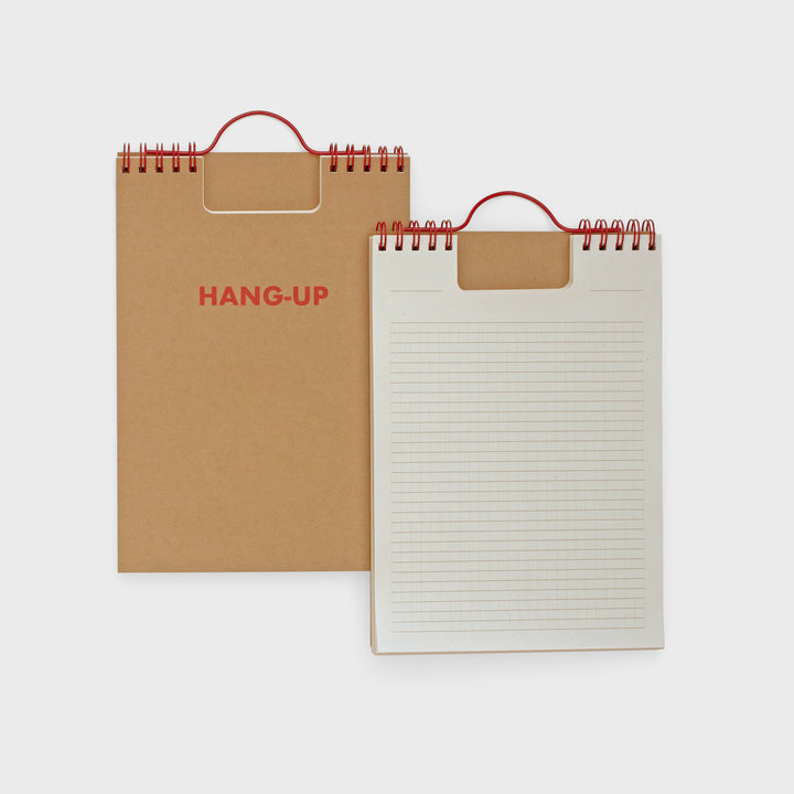 Two spiral-bound notebooks, one brown with 'HANG-UP' text and one white with lined pages, on a light gray background.