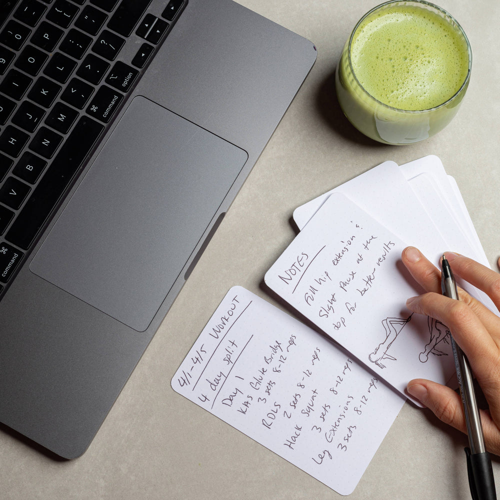 Laptop, glass of green juice, and handwritten notes on a desk.