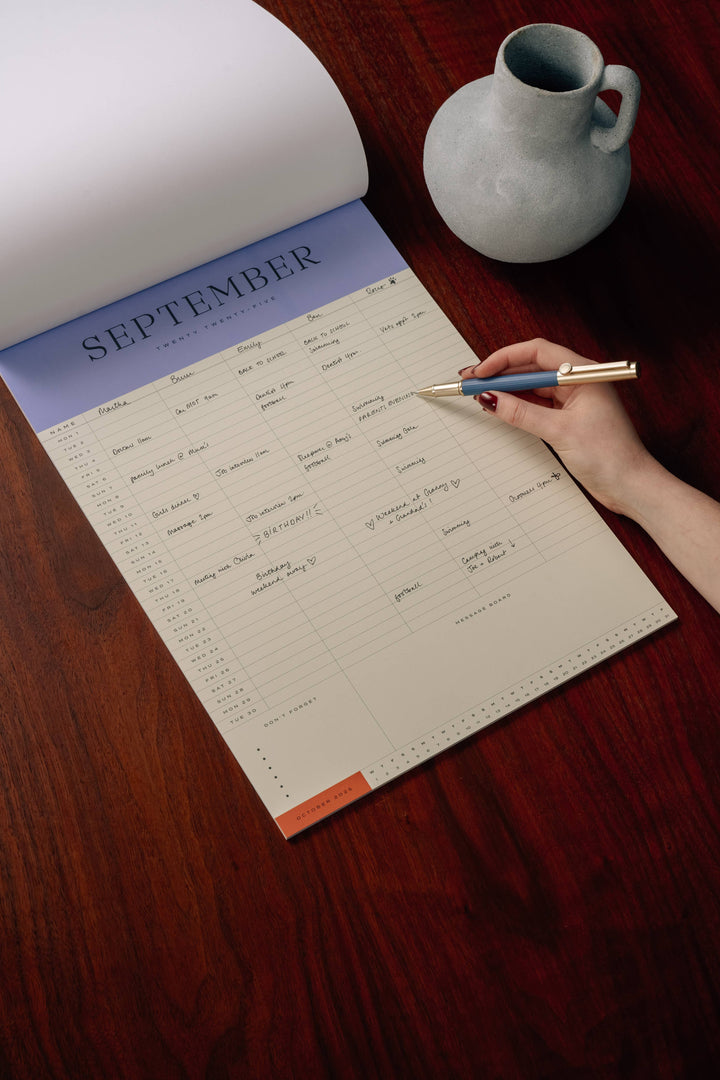 Person writing on a September calendar with a pen on a wooden surface