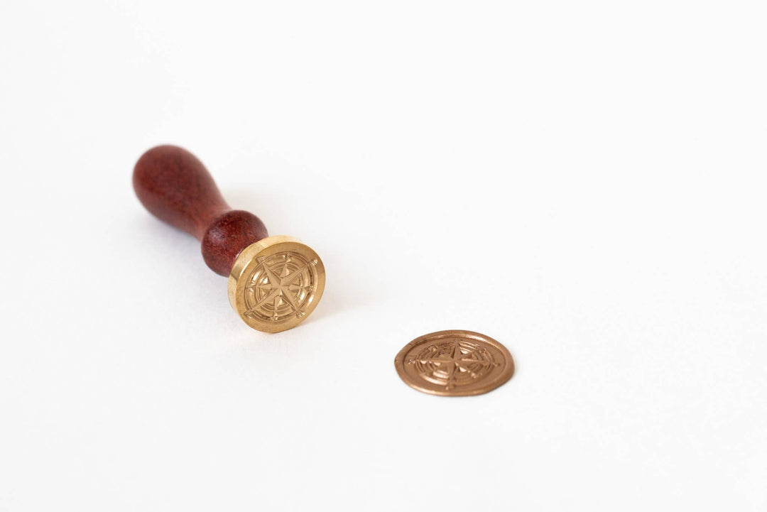 Gold wax compass seal with wooden handle on a white background