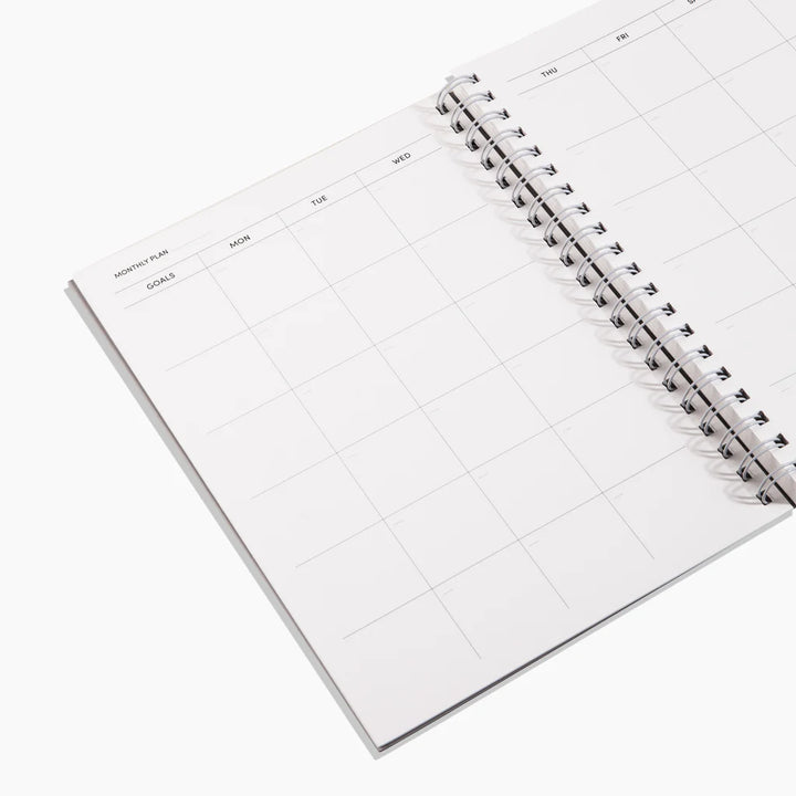 Open spiral-bound planner with grid layout on a white background
