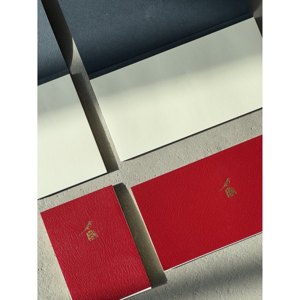 Two red notebooks with gold symbols on a textured surface