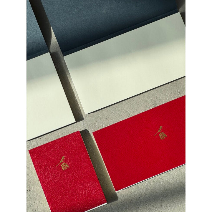 Two red notebooks with gold symbols on a textured surface