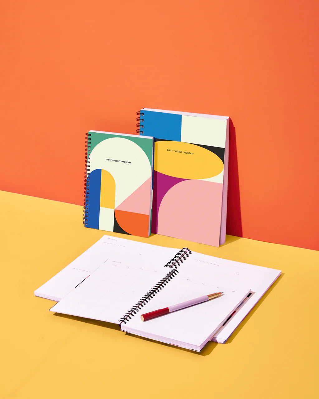 Colorful spiral-bound notebooks with abstract designs on an orange and yellow background