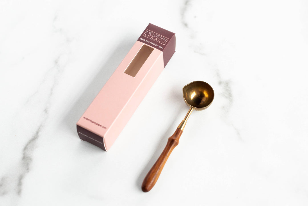 Gold wax melting spoon next to its packaging on a marble surface