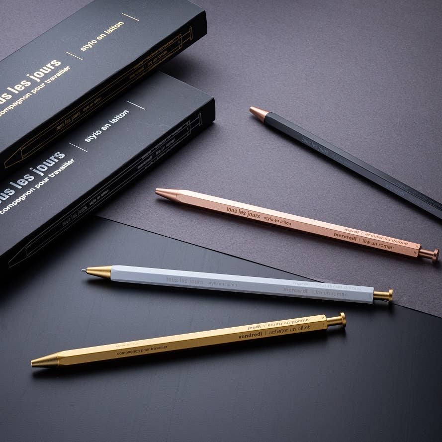 A selection of ballpoint pens with brass bodies, available in gold, silver, and rose gold colors, displayed alongside their packaging boxes.