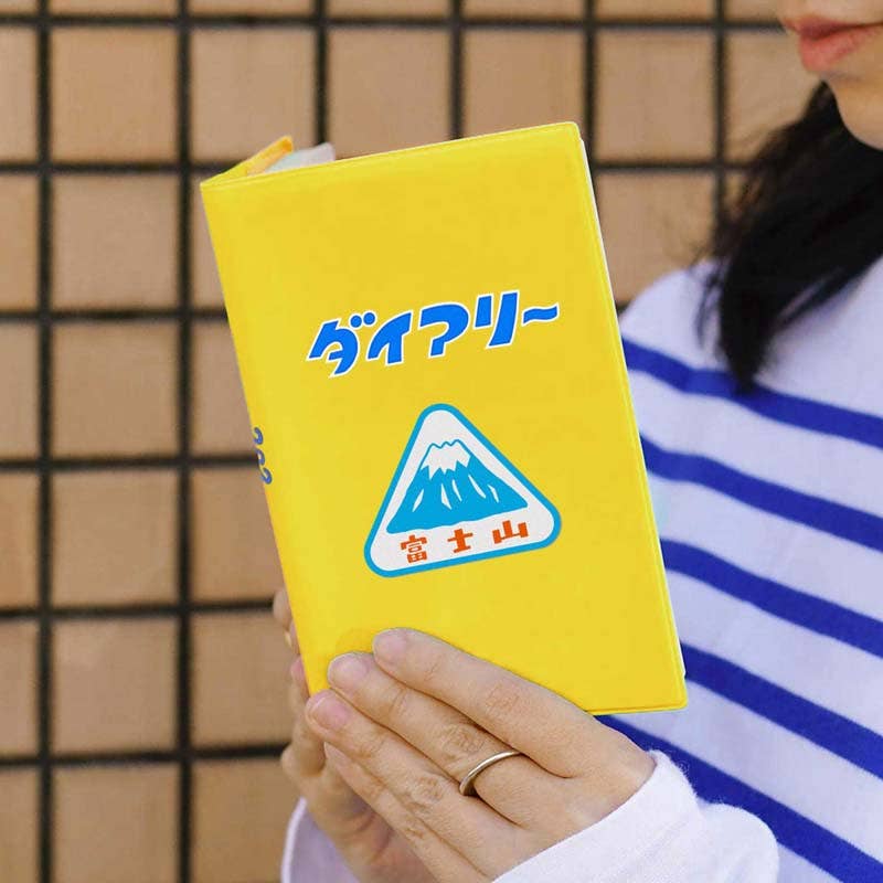 Yellow diary with Mount Fuji design held by a person wearing a striped shirt.