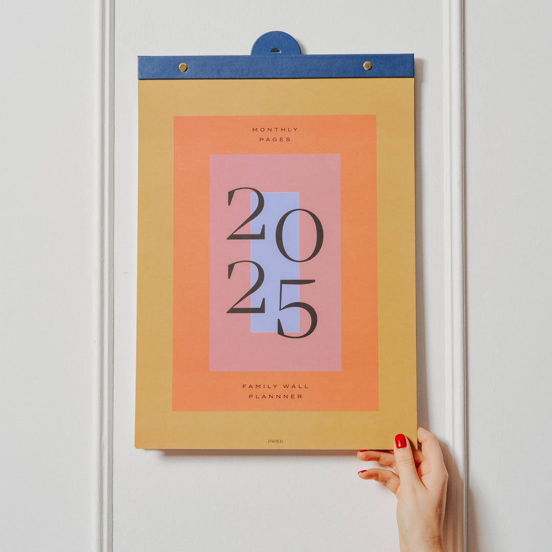 Calendar with '2025' design on a white wall, held by a hand.