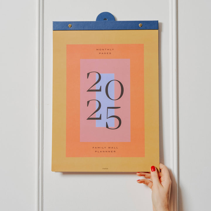 Calendar with '2025' design on a white wall, held by a hand.
