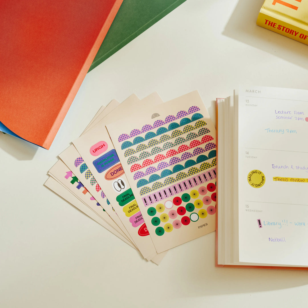 Colorful sticker sheets on a table with books in the background