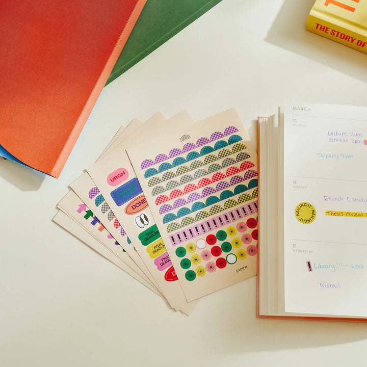 Colorful sticker sheets on a table with books in the background