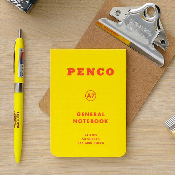 Yellow Penco notebook with a pen and clip on a wooden surface