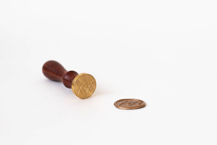 Gold wax xoxo stamp with wooden handle on a white background
